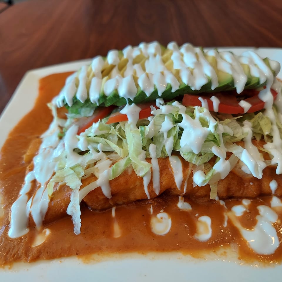 Enchiladas covered in red sauce, topped with shredded lettuce, sliced tomatoes, avocado, and sour cream.