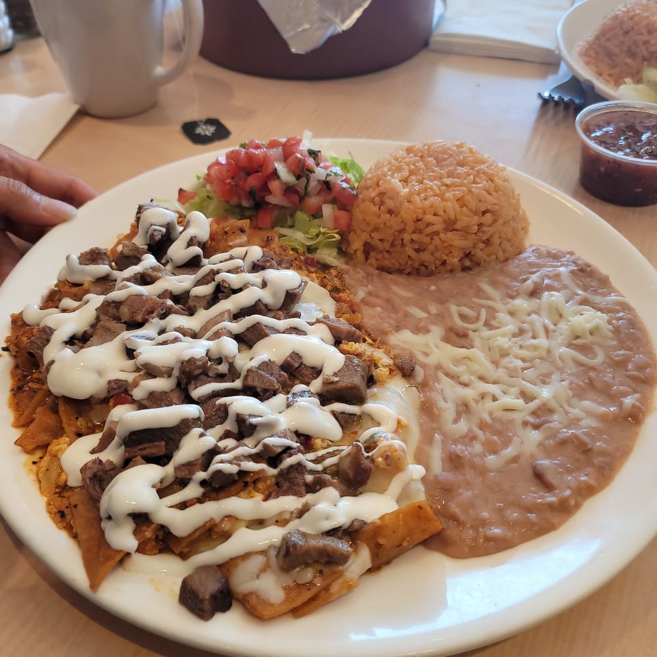 A plate of chilaquiles with steak, crema, rice, refried beans, and pico de gallo.