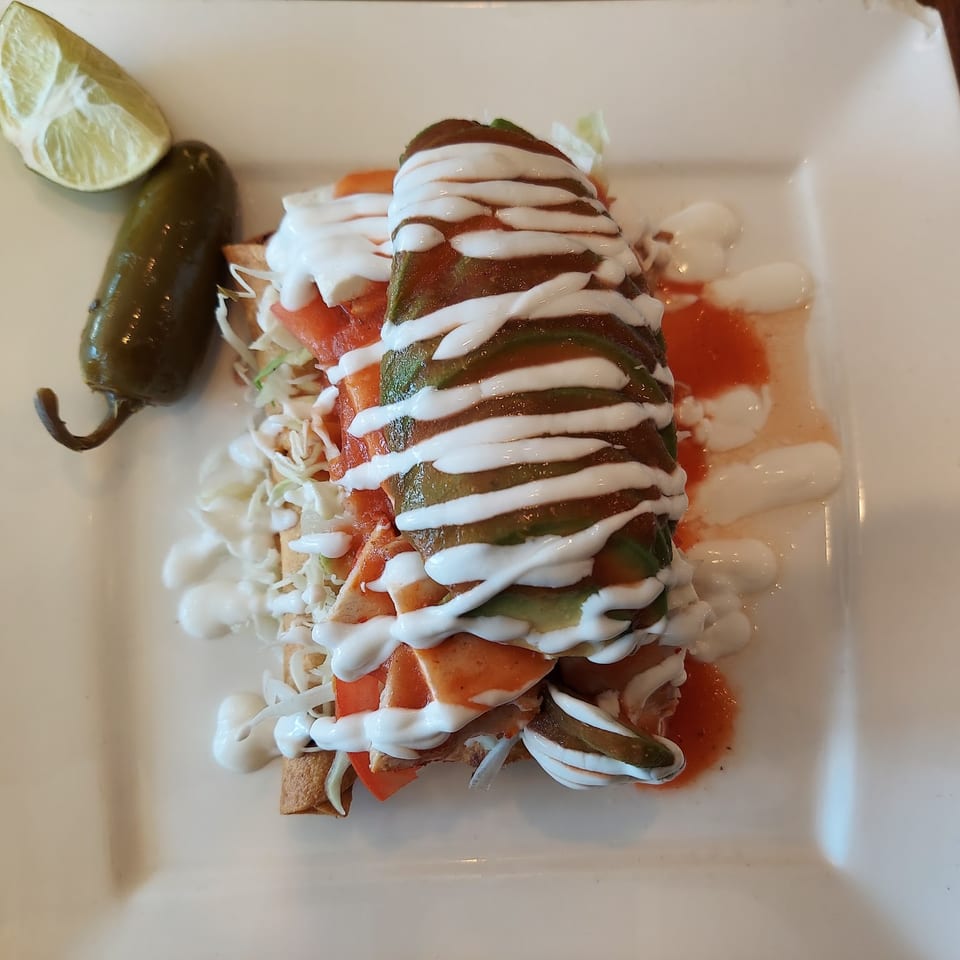 A plate of Mexican food with a crispy shell, topped with avocado, sour cream, and salsa.