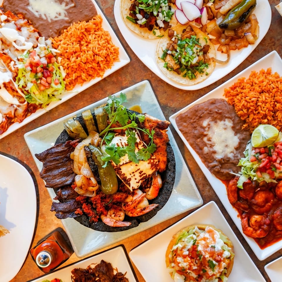 Overhead view of a table laden with various vibrant Mexican dishes, including tacos, enchiladas, and shrimp.