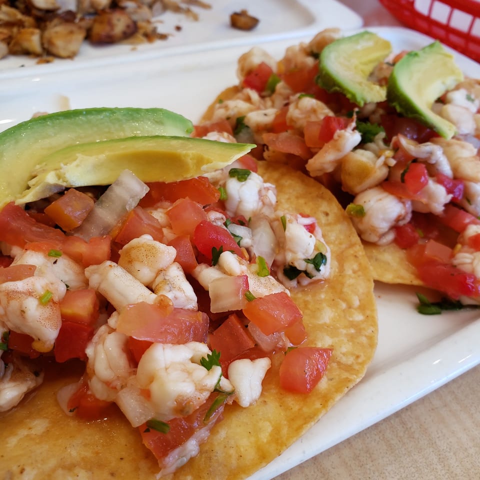 Two shrimp ceviche tostadas topped with diced tomatoes, onions, and avocado slices.