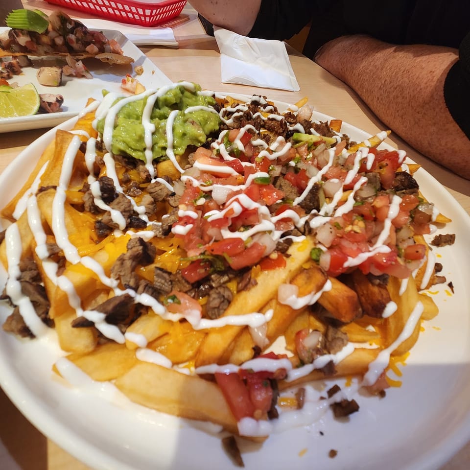 Loaded fries with steak, cheese, guacamole, pico de gallo, and sour cream on a white plate.